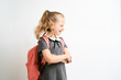 © briagin - Little girl photographed against white background wearing school uniform dress isolated holding a coral backpack on both shoulders