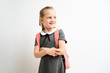 © briagin - Little girl photographed against white background wearing school uniform dress isolated holding a coral backpack on both shoulders