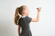 © briagin - Little girl photographed against white background wearing school uniform dress isolated is mocking writing with marker