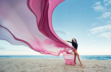 Slim Woman at the beach with long pink fabric. Sky background at the summer. Classic dancer on the nature 