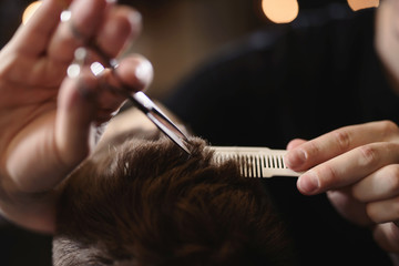 Close up barber's hands cuts hair with scissors and beard of men in the barbershop, hairdresser makes hairstyle for a young man