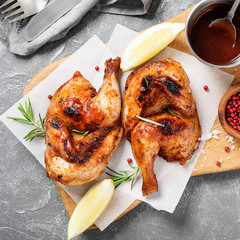 Wall Mural - Halves of appetizing grilled juicy chicken with golden brown crust served with lemon slices,barbeque  sauce and rosemary.