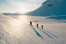 Three Hikers With Shadows Are Skitouring In Norway Landscape In Sunset.