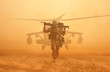 Military soldier walking at desert with gun on his shoulder in front of helicopter in sand storm.