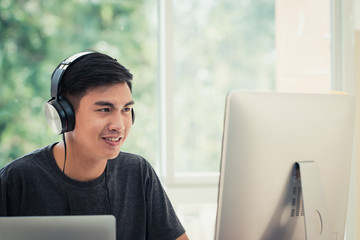 Wall Mural - student learning online study concept: asian young man listening with headphones and laptop, sitting