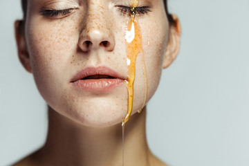 Closeup portrait of beautiful young brunette woman with freckles and honey on face with closed eyes and serious face. indoor studio shot isolated on gray background.