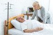 © LIGHTFIELD STUDIOS - smiling senior woman standing near ill husbend in hospital