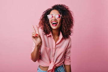 Blissful lovable woman with african hairstyle laughing during indoor photoshoot. Graceful cute girl in romantic casual clothes enjoying leisure time in studio.