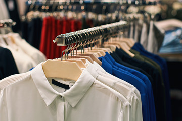 Wall Mural - Woman shirts amd blouses in white, blue, black and other colors on hangers in a retail clothes store.