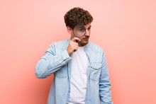 Blonde Man Over Pink Wall Taking A Magnifying Glass And Looking Through It