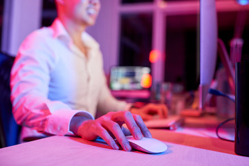 Wall Mural - Close-up of young manager sitting at the table working on computer and using wireless computer mouse in dark office