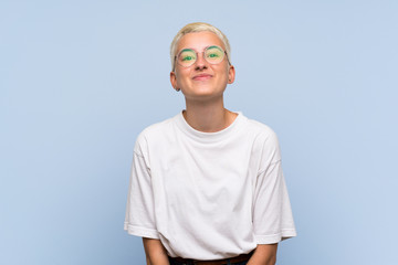 teenager girl with white short hair over blue wall with glasses and smiling