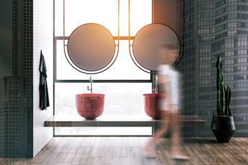 Woman walking in gray bathroom with sinks