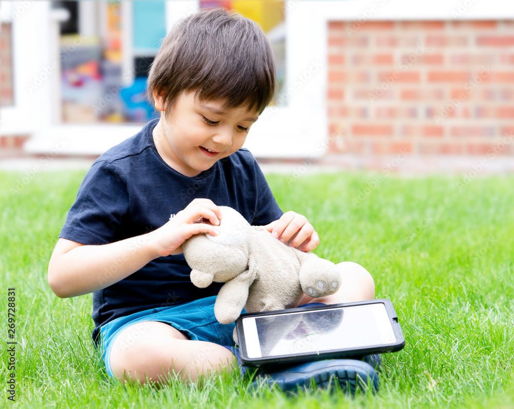 Cute little boy watching his tablet and playing with teddy bear in the ...