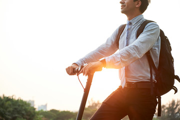 Young office worker with backpack behind his back using scooter as a means of transportation on the street, he coming back from work