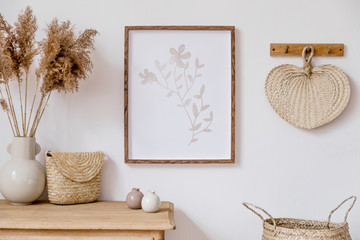 Stylish korean interior of living room with brown mock up poster frame, elegant accessories, flowers in vase, wooden shelf and hanging rattan leaf. Minimalistic concept of home decor. Template. 