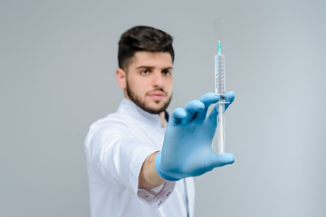 Wall Mural - Suringe in focus, middle eastern medical doctor in gloves on background isolated over grey wall