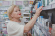 © Ihor - Charming senior lady smiling, picking cosmetic or medical products from a shelf at drugstore. Lovely elderly female customr shopping at the pharmacy. Seniority, consumerism concept