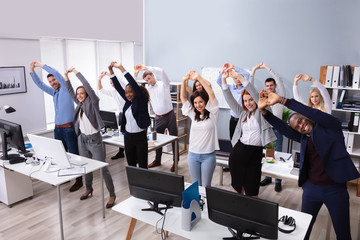 Wall Mural - Young Businesspeople Doing Stretching Exercise At Workplace