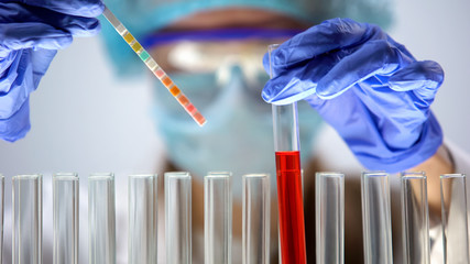 researcher measuring ph level in red liquid substance with litmus paper, test