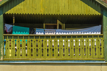  Green painted wooden balcony of the house with laundry on a sunny hot summer day. The front of the balcony is decorated with geometric patterns wood carvings