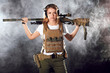 Woman soldier in military camouflage uniform protected with helmet, body armour, holding assault rifle standing against dark smoky background