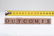 Outcomes Block With Measurement Tape On Reflective Desk