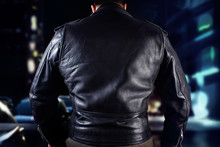 Biker man in leather jacket standing on night city street back view.