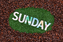 Close Up Of Word Sunday On Grass With Coffee Beans Around