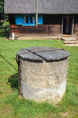 Poster - Old well in front of wooden cottage in heritage park in Olsztynek town of Olsztyn County in Warmia-Mazury Province, Poland