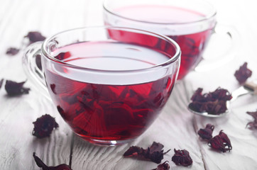 Closeup view at two tea cups and dry hibiscus petals on white wooden table background