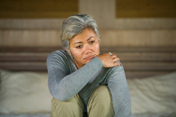 dramatic lifestyle home portrait of attractive sad and depressed middle aged woman with grey hair on bed feeling upset suffering depression and anxiety