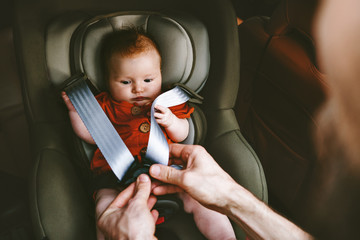 Baby sitting in safety car seat and father fastens belt happy family lifestyle vacation road trip child security transportation