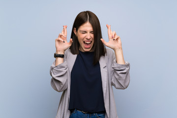 Wall Mural - Young woman over isolated blue wall with fingers crossing