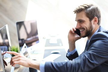 Modern businessman analyzing data using computer and talking on the phone while sitting in the office.