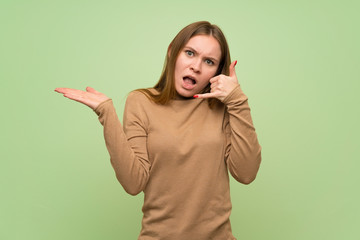 Young woman with turtleneck sweater making phone gesture and doubting