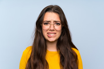 Wall Mural - teenager girl over isolated blue wall having doubts and with confuse face expression