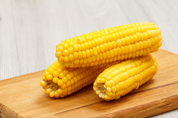 Cutting board with boiled corn on a table.