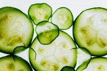 Green Translucent Slices Of Cucumber On The Background Of Bright White Light Close-up. Transparent Discs Of Vegetables. Texture Of Kaleidoscope Patterns In Macro
