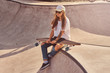 © Fxquadro - Beautiful young woman in sunglacces and cap is sitting at skatepark on the ramp with her longboard.