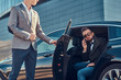 © Fxquadro - Attractive serious man in sunglasses is talking by smartphone and sitting in the car while his assistant is opening door for him.