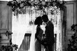 © Wedding photography - Wedding ceremony. Elegant wedding couple kissing near wedding arch. Black and white photo of bride and groom in love