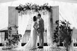 © Wedding photography - Wedding ceremony. Elegant wedding couple kissing near wedding arch. Black and white photo of bride and groom in love