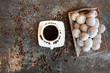 Czarna kawa w białej filiżance obok tacy z mini pączkami posypanymi cukrem pudrem