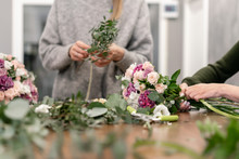 Close-up Flowers In Hand. Florist Workplace. Woman Arranging A Bouquet With Roses, Carnation And Other Flowers. A Teacher Of Floristry In Master Classes Or Courses