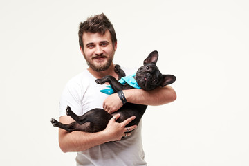 Hipster Bearded guy holding and hugging a nice French Bulldog dog in his arms with love and playing with him, against a white background