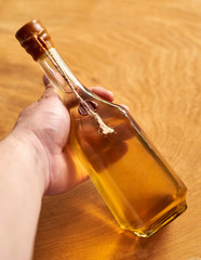 Homemade sweet alcoholic drink based on honey and lemon, a bottle in hand on a wooden background