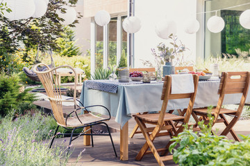 Wall Mural - Table with wooden chairs in bright green garden of modern house, real photo