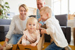 © Seventyfour - Positive playful young family with two children having fun in new flat: pretty little girl sitting in moving box and looking at camera while other family members looking inside this box