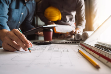 Two colleagues discussing data working and tablet, laptop with on on architectural project at construction site at desk in office